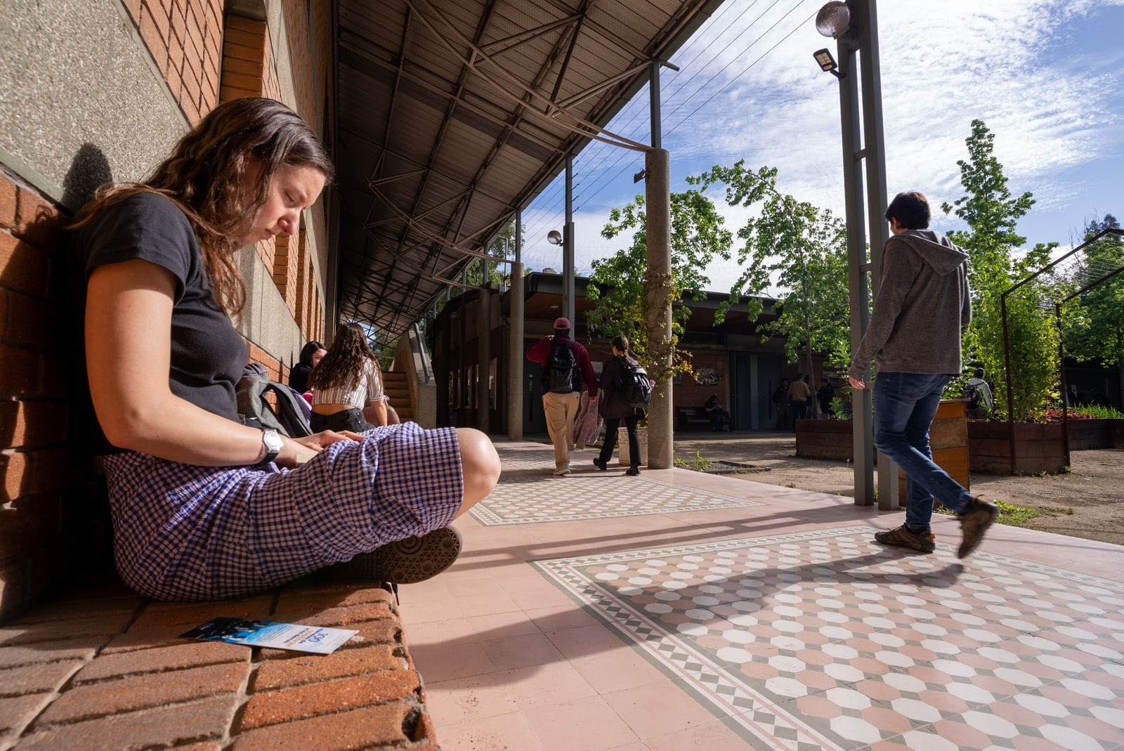 Estudiante sentada en un banco, usando su teléfono en el campus.